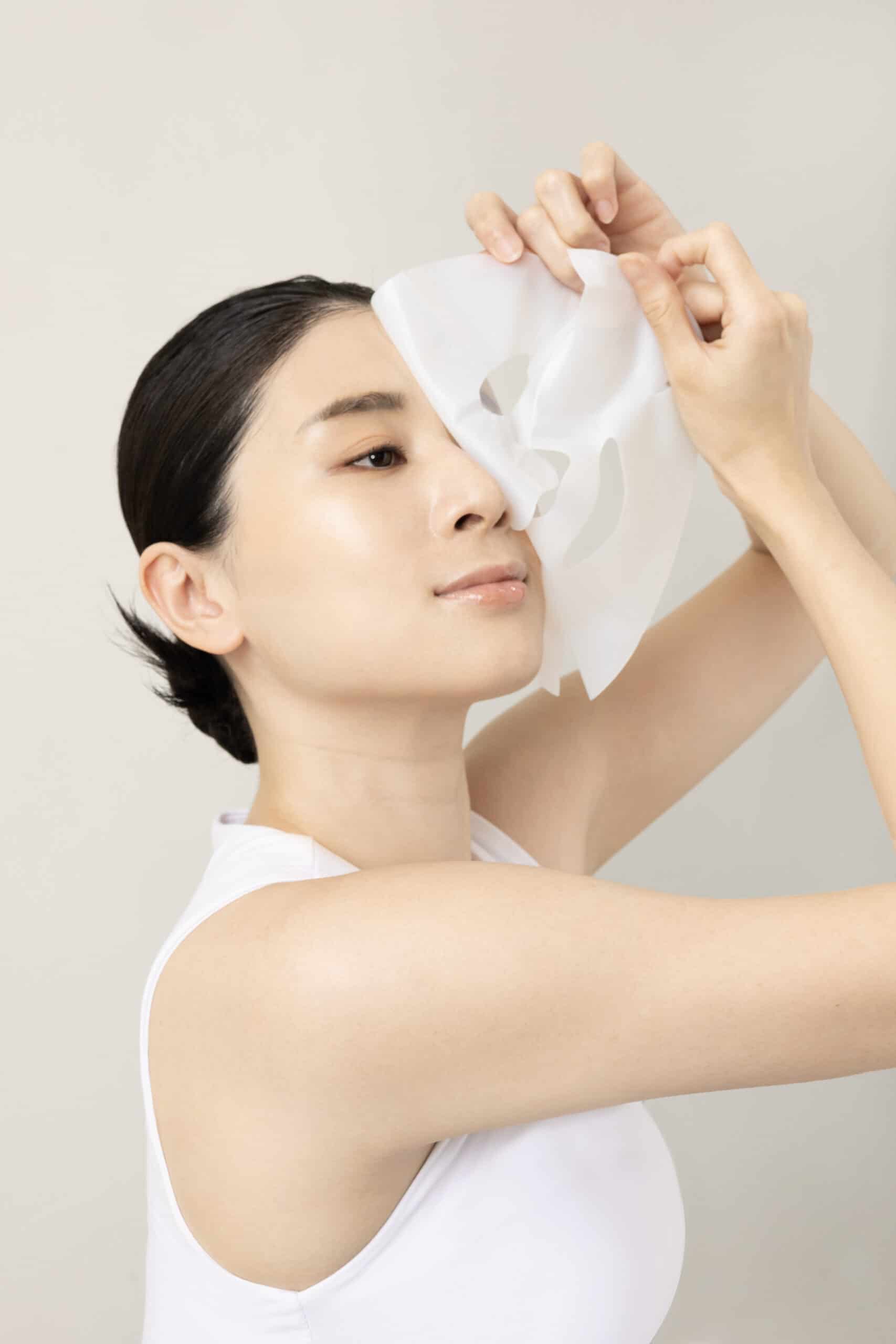 Elegant woman holding a white facial mask for skincare product display.