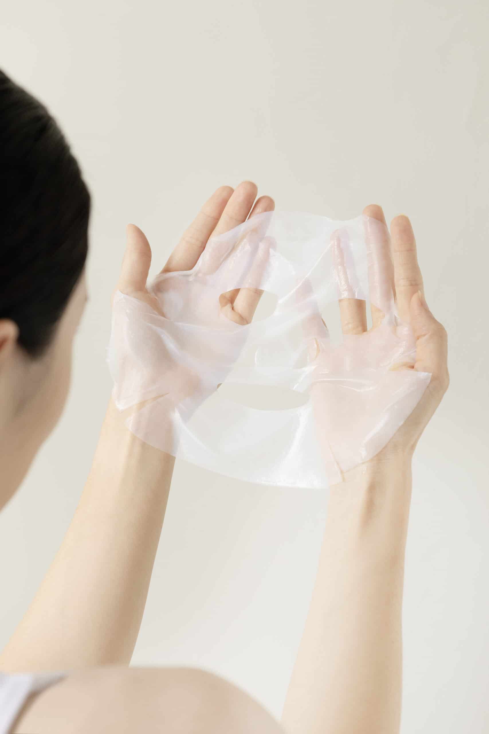 Hand holding a white skincare sheet mask for e-commerce product photography.
